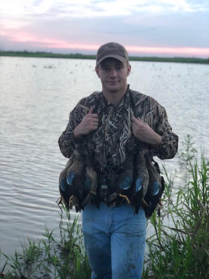 Young hunter with a strap of ducks on the water's edge