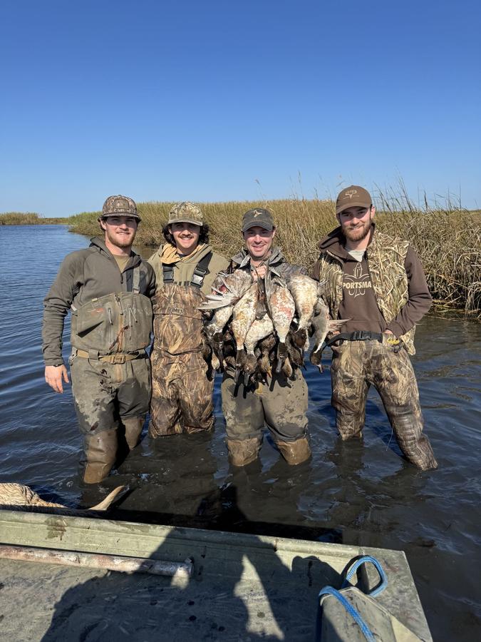 Four hunters standing in flooded marsh with the morning's ducks